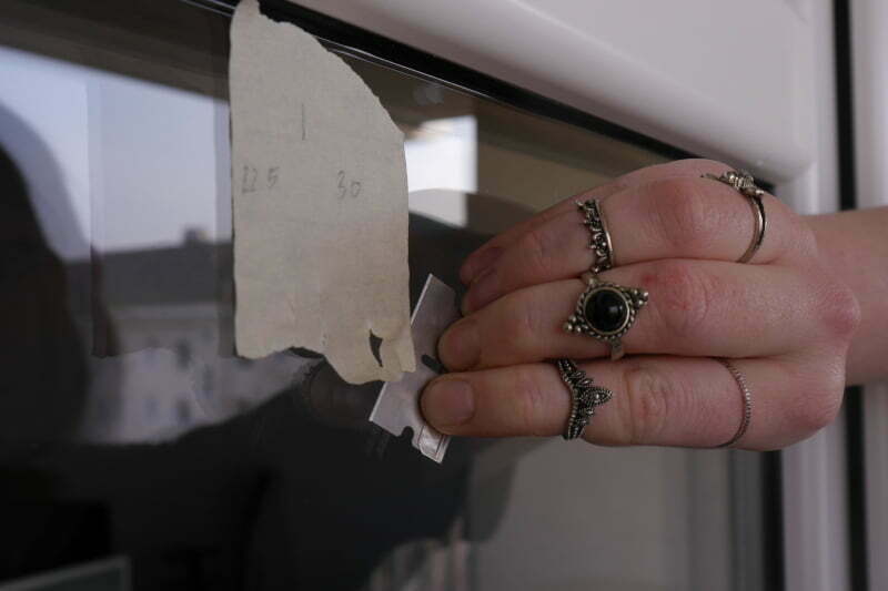 Mit einer Klinge wird ein Klebestreifen von einer Fensterscheibe gelöst