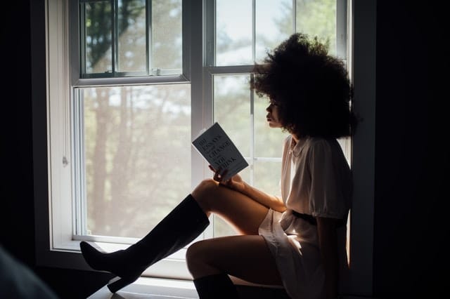 Eine Frau sitzt an einem Fenster und liest ein Buch