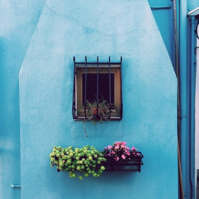 An einer blauen Wand befindet sich ein Fenster, welches mit Gitterstäben gesichert ist