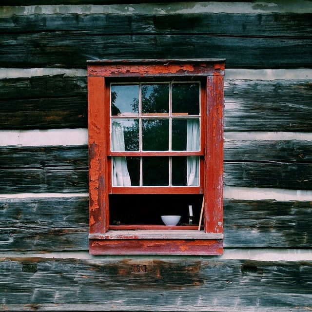 Ein Fenster mit einem roten Holzrahmen ist einen Spalt weit geöffnet