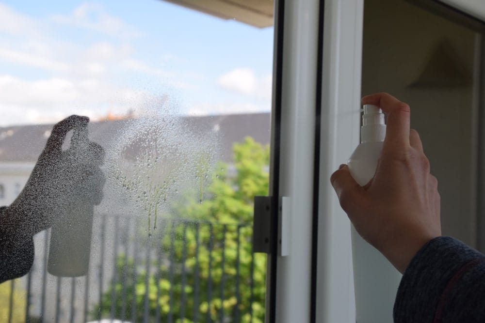 Jemand sprüht eine Fensterfolie mit Glasreiniger ein