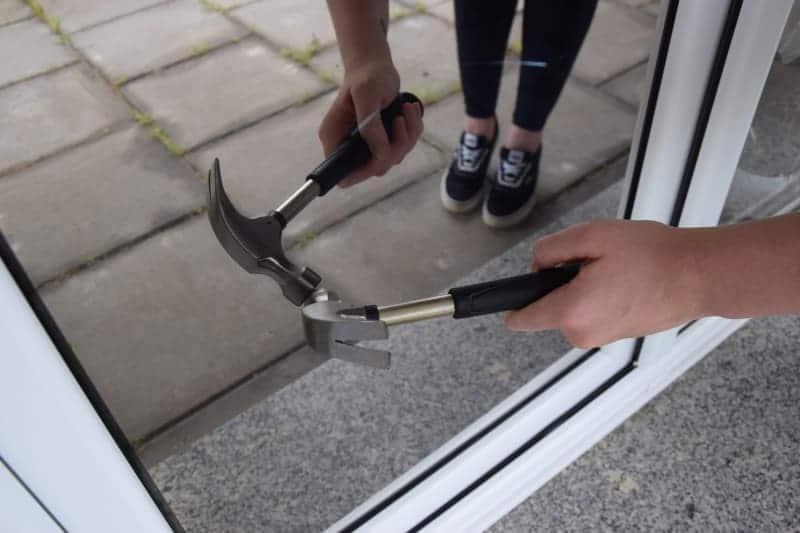 Eine Person versucht mit einem Hammer, ein Fenster einzuschlagen.