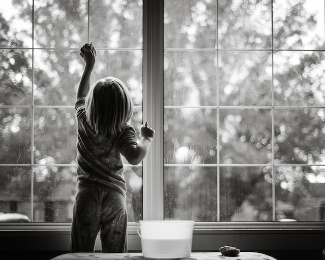 Ein Kind steht vor einer großen Fensterfront und wischt diese mit einem Lappen ab