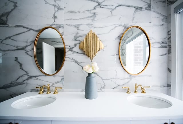 Hinter einem Waschbecken und zwei ovalen Spiegeln sind gemusterte weiß-schwarze Fliesen angebracht