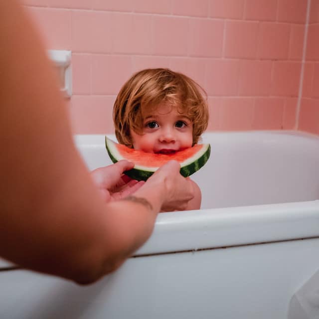Ein Kind sitzt in einer Badewanne, dahinter einige rosa Fliesen