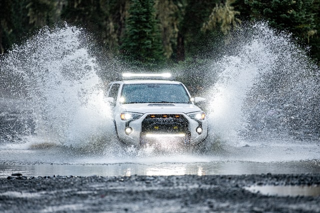 Ein weißes Auto fährt durch Wasser und spritzt Fontänen