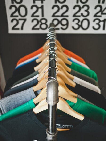 Verschiedenfarbige T-Shirts hängen auf Holzbügeln auf einer Kleiderstange