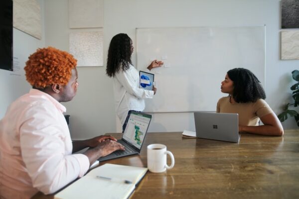 Drei Menschen arbeiten gemeinsam mit Laptops und Whiteboard an einem Projekt