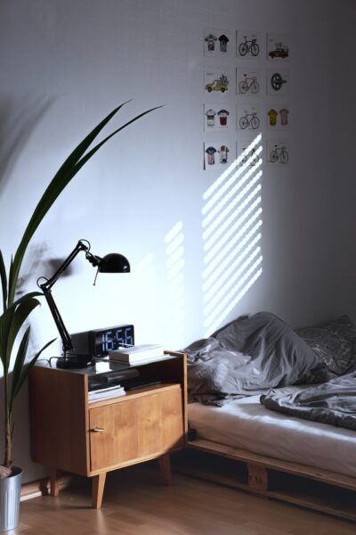 Mit einigen Hilfsmitteln schaffen Sie eine gute Schlafatmosphäre Ein Bett neben dem ein Beistelltisch steht und auf das ein Lichtstrahl scheint