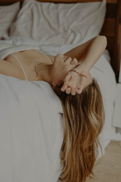Wenn der Körper nicht zur Ruhe kommt, kann das gravierende Folgen haben Eine Frau liegt auf einem Bett und hält sich einen Arm vor die Augen