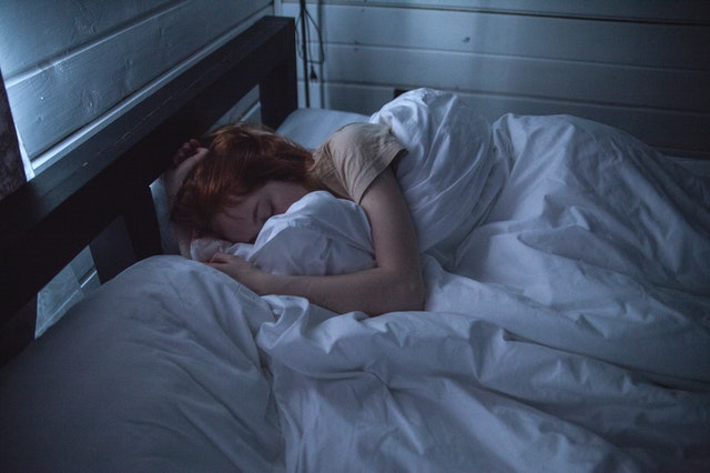 Eine Frau liegt eingekuschelt in ein weißes Bett