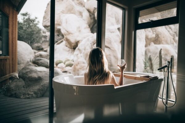 Eine Frau sitzt in einer Badewanne, vor ihr eine große Fensterfront
