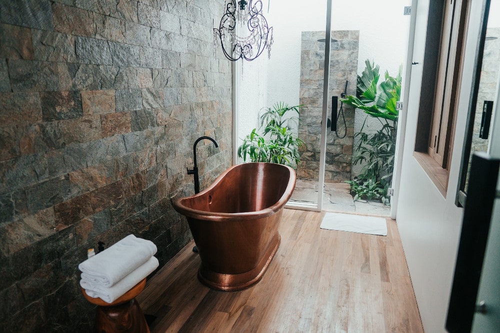 Ein Bad dessen Wand mit braunen Naturfliesen verkleidet wurde und in dessen Mitte eine kupferfarbene Wanne steht