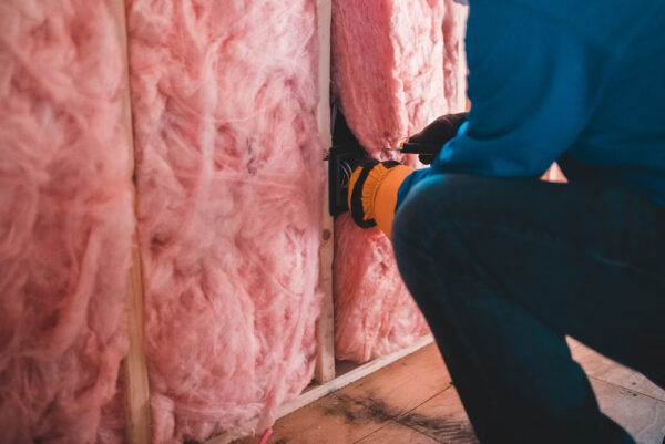 Jemand dämmt eine Wand mit pinker Isolierwolle