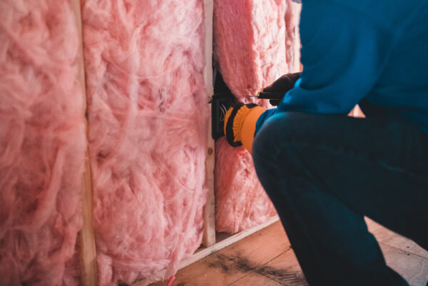 Wände können nachträglich isoliert werden, aber das ist aufwendig Jemand dämmt eine Wand mit pinker Isolierwolle