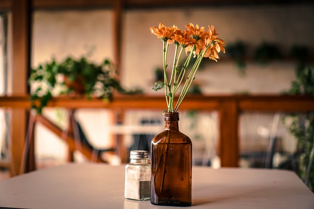 Eine braune Glasflasche mit Blumen steht zusammen mit einem Pfefferstreuer auf einem Tisch