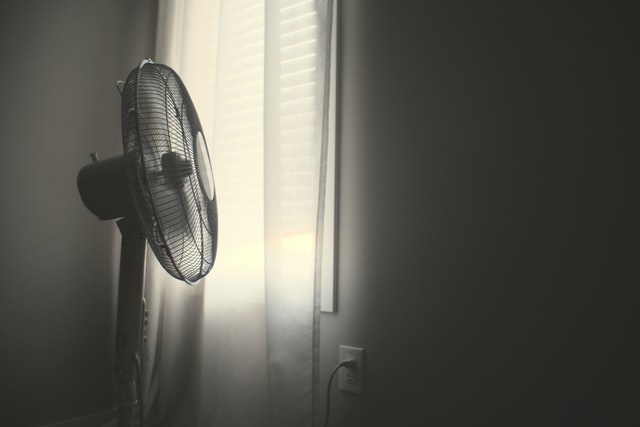 Ein Ventilator steht vor einem Fenster mit dem Vorhang