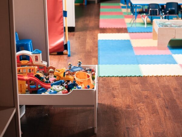 Ein Raum mit buntem Teppich. Im Vordergrund ist ein Regal mit Spielzeug