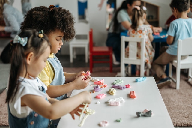 Zwei Kinder spielen mit Knete an einem niedrigen Tisch. Weiter Kinder im Hintergrund