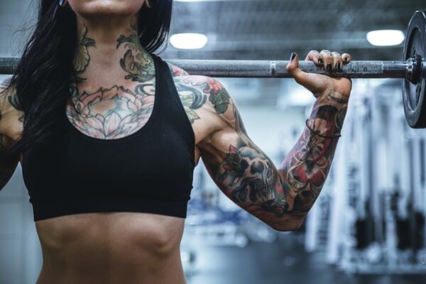 Denken Sie an die Kosten, die beim Fitnessraum einrichten entstehen Tätowierte Frau stemmt Gewichte