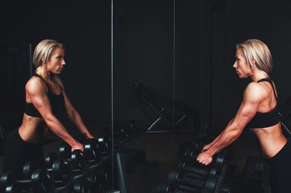 Denken Sie beim Fitnessraum einrichten auch an die Wände Frau, die trainiert, betrachtet sich im Spiegel