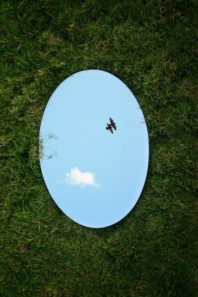 Im Gras liegt ein Spiegel, der den Himmel reflektiert