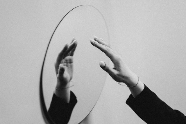 Schwarz-weiß-Bild von einem Spiegel, in dem sich eine Hand spiegelt