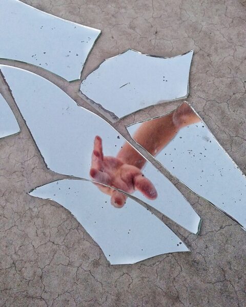 Ein zerbrochener Spiegel, in dem eine Hand zu sehen ist
