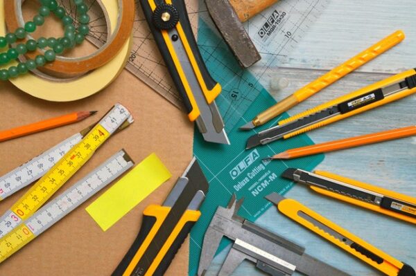 Auf einem Tisch verstreut liegen Bleistifte, Lineale, eine Schneidematte und Teppichmesser