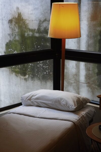 Mit Schimmel, der durch Feuchtigkeit entsteht, ist nicht zu spaßen Ecke eines Fensters, davor eine Lampe und ein Kissen, man sieht Feuchtigkeit und Schimmel