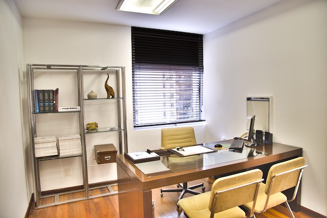 Ein simpel eingerichtetes Arbeitszimmer mit Regal, Schreibtisch und Stühlen