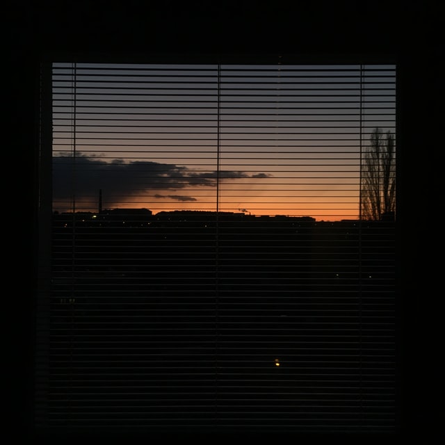 EIn Fenster mit Jalousie, im Hintergrund ist ein Sonnenuntergang