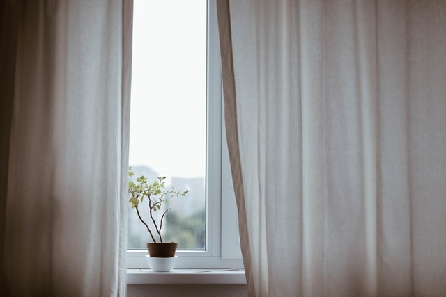 Ein weißer Vorhang, eine Pflanze steht im Fenster