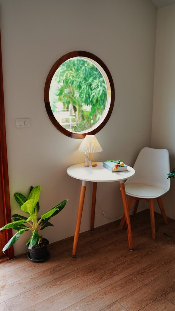 Ein kleiner Tisch und Stuhl stehen neben einem runden Fenster mit Holzrahmen