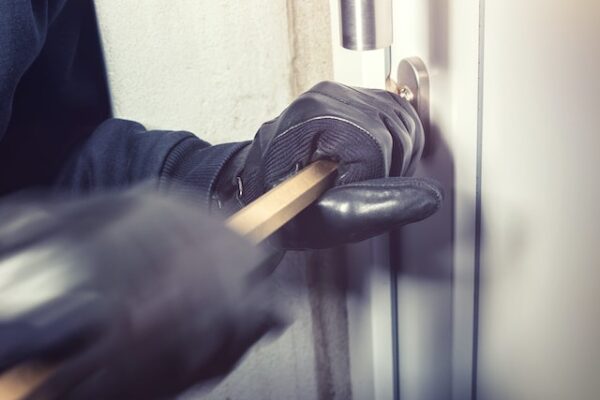 Eine Person mit Handschuhen versucht mit einem Brecheisen ein Fenster aufzustemmen