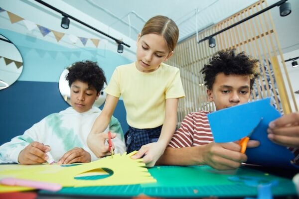 Basteln zu Ostern mit Folien klappt besonders gut. Drei Kinder schneiden etwas aus buntem Papier aus