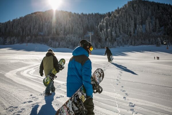 Schützen Sie sich auch im Winter angemessen Drei Personen laufen mit Snowboards unter dem Arm durch Schnee