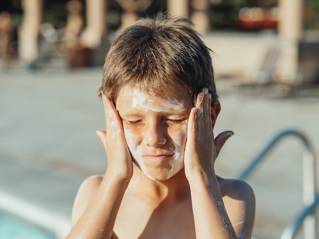 Ein Junge reibt sein Gesicht mit einer großzügigen Menge Sonnencreme ein