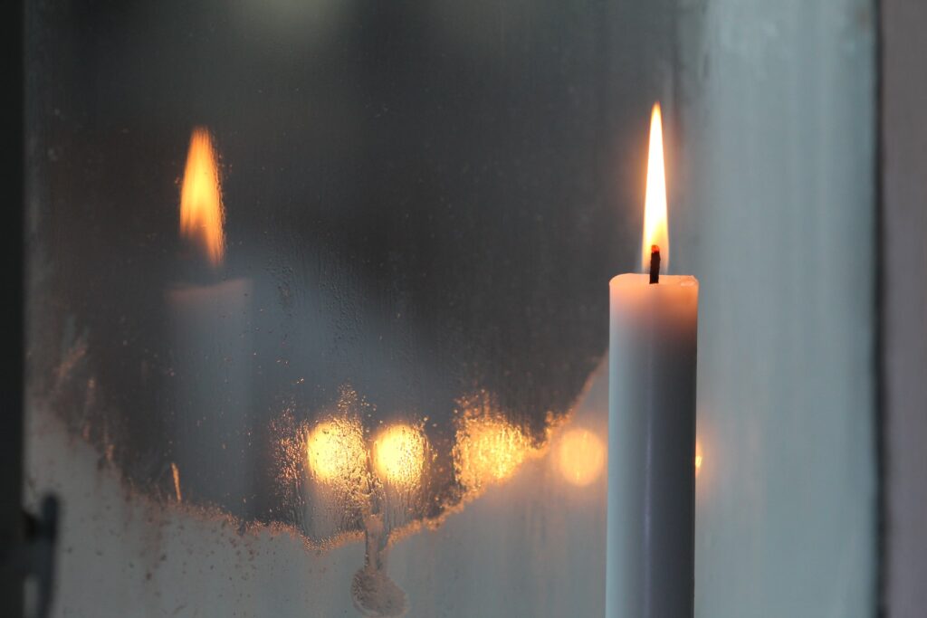 Eine Kerze brennt vor einem beschlagenen Fenster