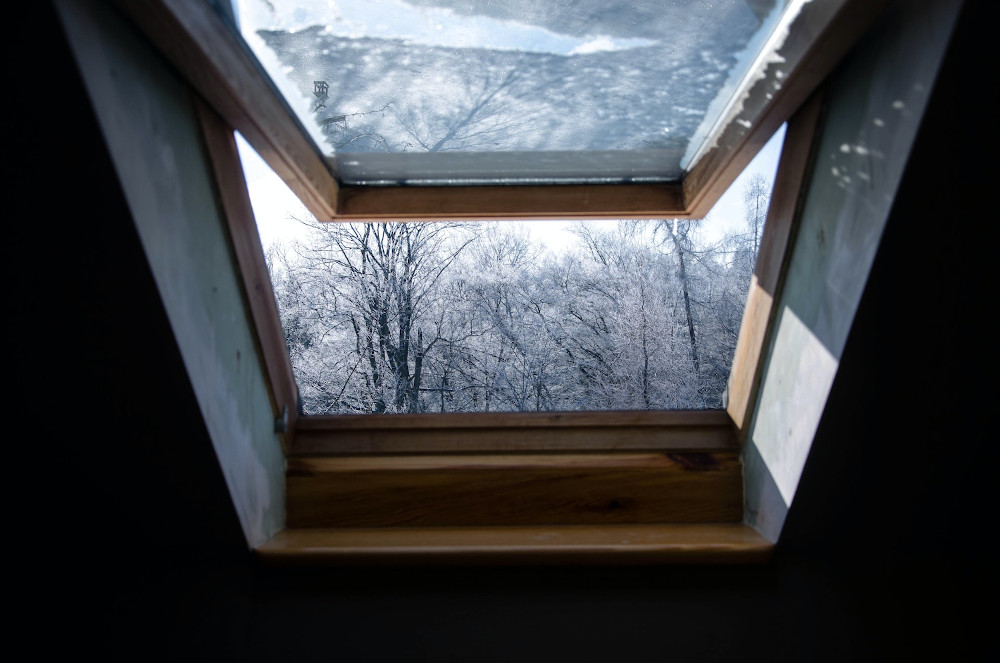 Ein offenes Dachfenster mit einer verschneiten Landschaft dahinter
