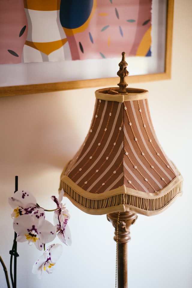 Eine Stehlampe mit altmodischem Lampenschirm aus braunem Stoffbezug vor einer Wand mit Bild