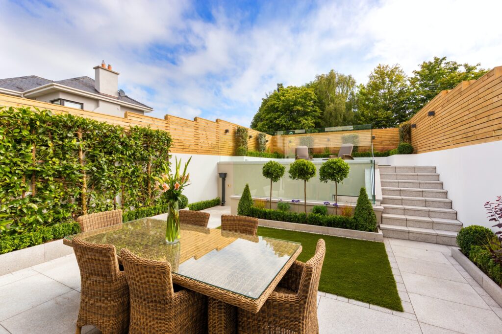 Eine Terrasse mit Tisch und Stühlen ist rundherum durch Begrünung sowie Holz- und Glaswände abgeschirmt