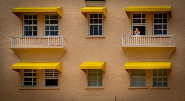 Eine einheitliche Schichtschutz-Idee für Balkon und Haus Eine Hauswand mit Fenstern, die alle über ein gelbes Rollo verfügen. Aus einem der Fenster lehnt ein Mann