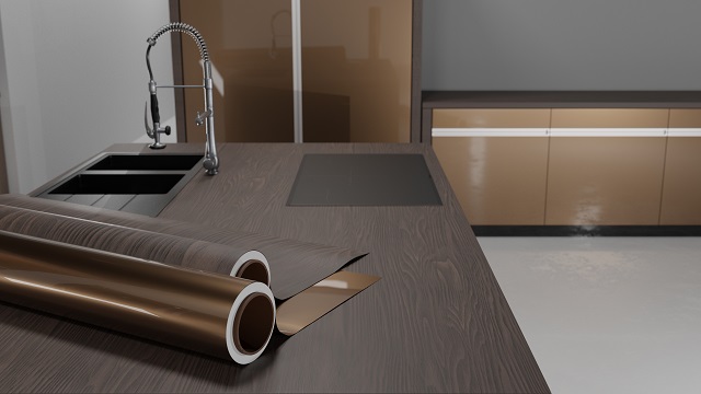 Auf einer Küchenarbeitsplatte aus dunkelbraunem Holz liegen zwei Rollen Möbelfolie, im Hintergrund sieht man auch eine Küchenzeile