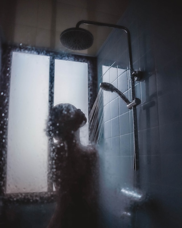 Unter einer laufenden Dusche hinter der leicht angelaufenen Scheibe ist der Umriss einer Frau zu erkennen
