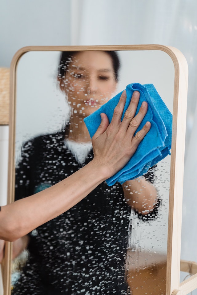 Eine Frau putzt einen Spiegel mit einem blauen Mikrofasertuch