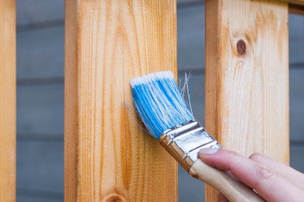 Eine Person bestreicht Holz mit einem Pinsel.