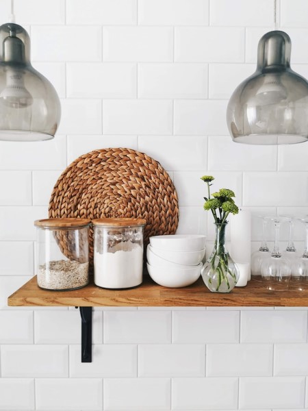 Eine weiß geflieste Küchenwand mit Regal, Lampen und Aufbewahrungsbehältern.