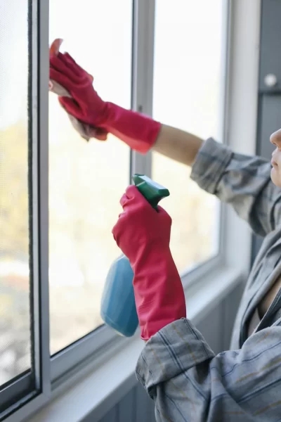Frau reinigt ein großes Fenster mit Spray und Handschuhen.