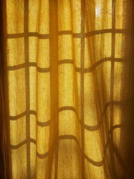 Licht fällt durch gelblichen Vorhang mit Schattenspiel